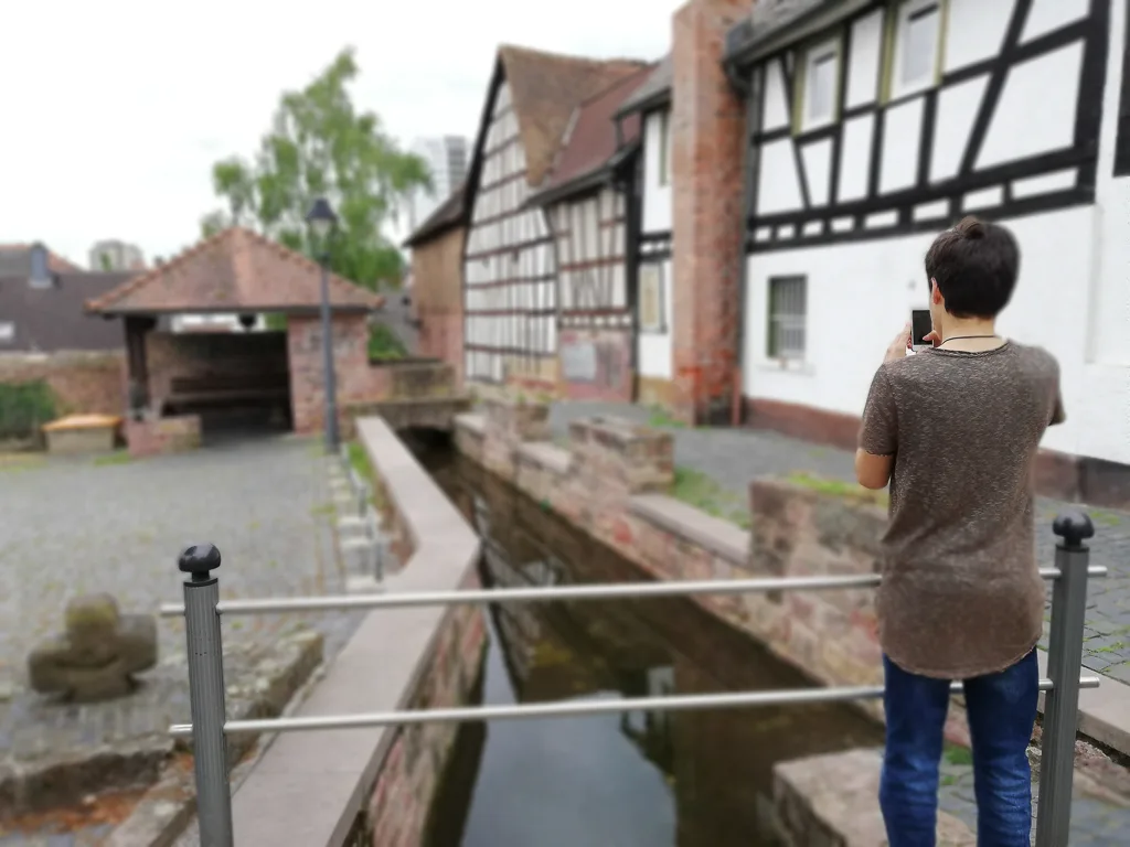 Jugendlicher fotografiert am Bachlauf vor Fachwerkhäusern.